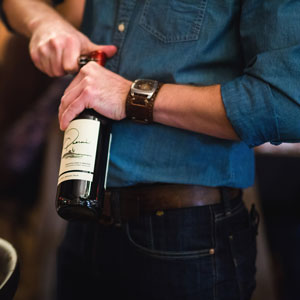 close-up of waiter in denim shirt opening a bottle of red wine